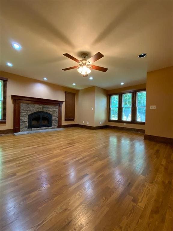 unfurnished living room with ceiling fan, a stone fireplace, and wood-type flooring