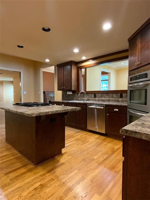 kitchen with backsplash, sink, light wood-type flooring, dark brown cabinetry, and stainless steel appliances