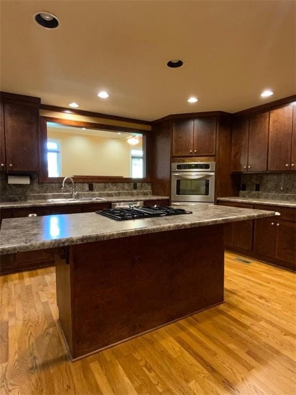 kitchen with dark brown cabinetry, sink, stainless steel appliances, and light wood-type flooring