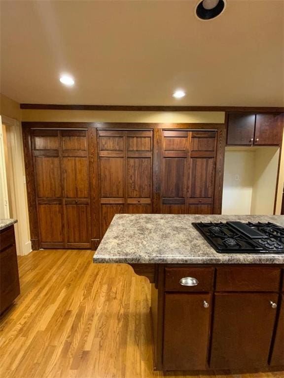 kitchen with light stone countertops, light wood-type flooring, black gas cooktop, and a breakfast bar area