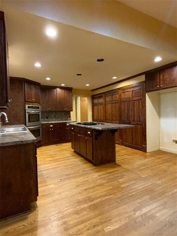 kitchen with dark brown cabinetry, stainless steel appliances, sink, light hardwood / wood-style floors, and a kitchen island