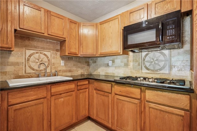 kitchen with decorative backsplash, black microwave, dark countertops, a sink, and stainless steel gas stovetop