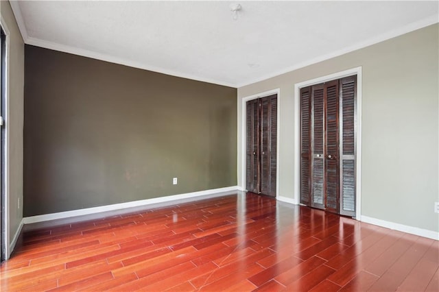 unfurnished bedroom with wood finished floors, ornamental molding, baseboards, and two closets