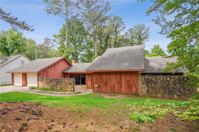 mid-century inspired home with board and batten siding, driveway, a chimney, an attached garage, and stone siding