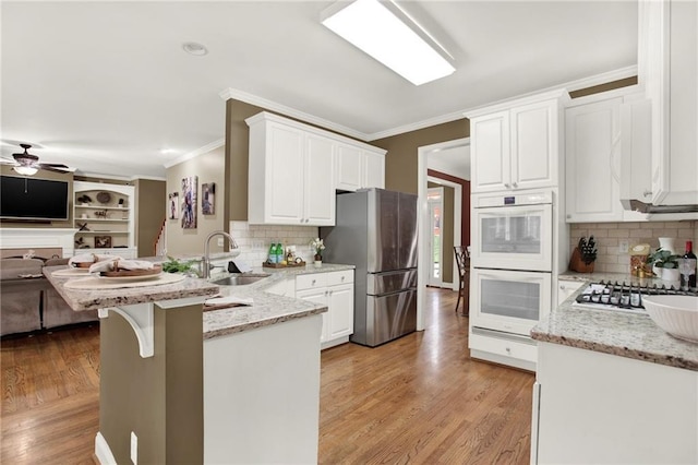 kitchen featuring sink, kitchen peninsula, stainless steel appliances, light stone countertops, and white cabinets