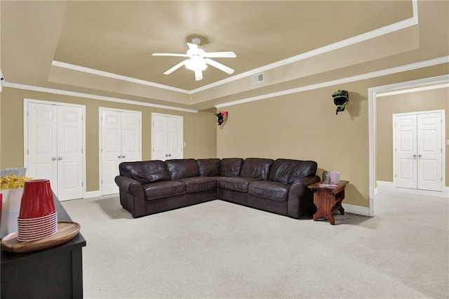 living room with a tray ceiling, ornamental molding, ceiling fan, and carpet