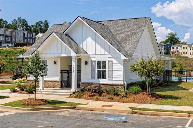 modern farmhouse featuring brick siding, board and batten siding, roof with shingles, and fence