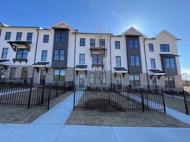 townhome / multi-family property featuring a fenced front yard, stucco siding, brick siding, and a standing seam roof