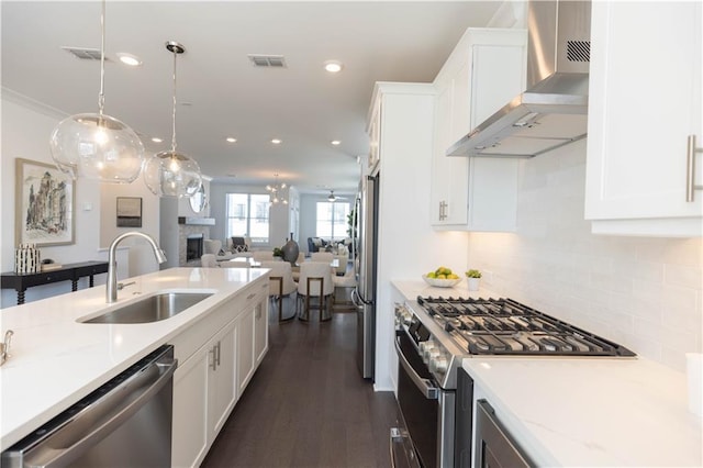 kitchen with appliances with stainless steel finishes, sink, wall chimney range hood, decorative light fixtures, and white cabinetry