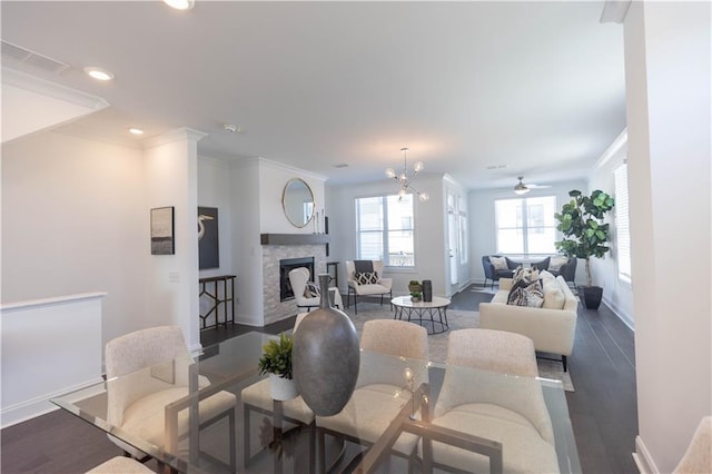 dining space featuring dark hardwood / wood-style flooring, ceiling fan with notable chandelier, a stone fireplace, and ornamental molding