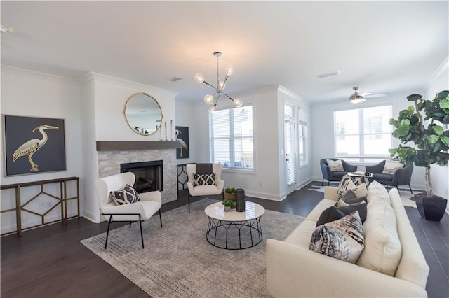 living room with a fireplace, ornamental molding, dark wood-type flooring, and ceiling fan with notable chandelier