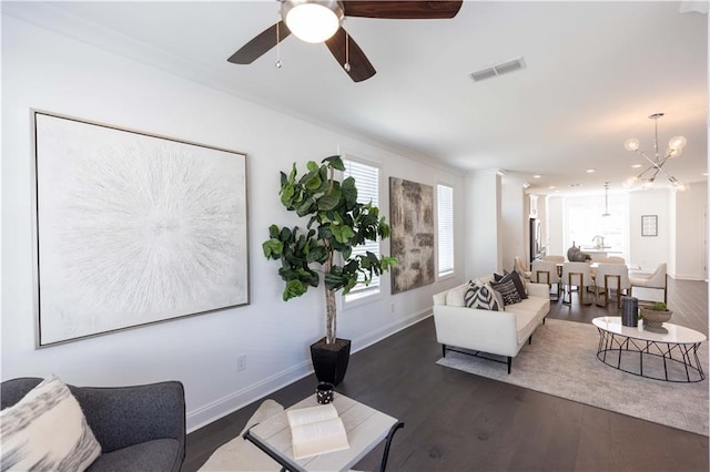 living room with ceiling fan with notable chandelier, crown molding, and dark wood-type flooring