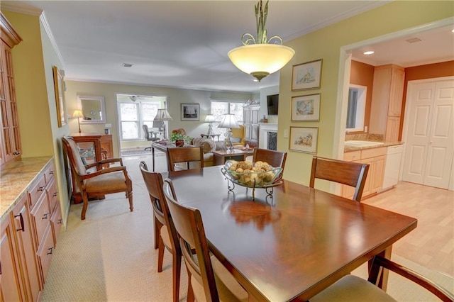 dining space featuring visible vents, a fireplace, crown molding, and light wood-style floors