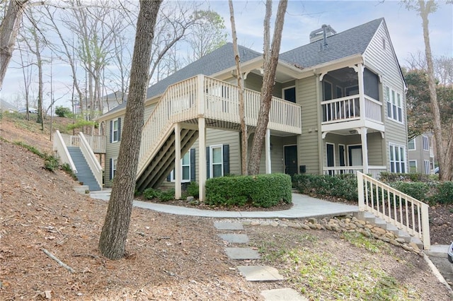 view of side of property with stairway, a chimney, and a shingled roof