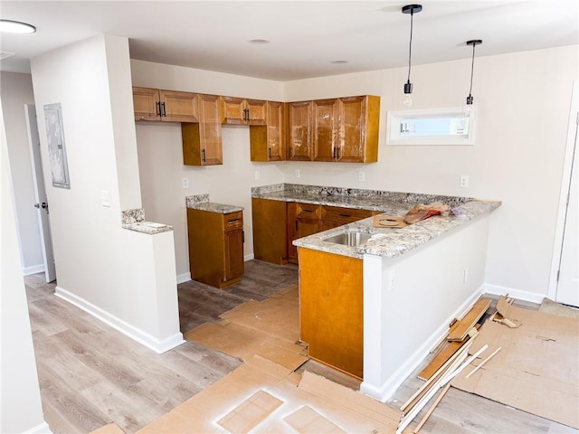 kitchen featuring pendant lighting, light stone counters, light hardwood / wood-style floors, and kitchen peninsula