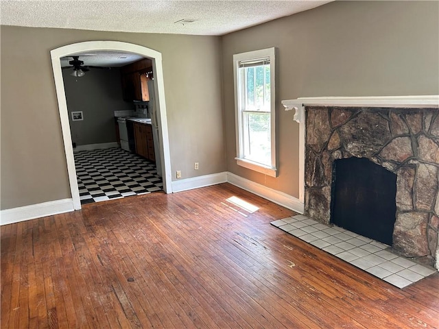 2203 Hillcrest Ave, Decatur, GA 30032 - unfurnished living room featuring a stone fireplace, a textured ceiling, light wood-type flooring, and ceiling fan