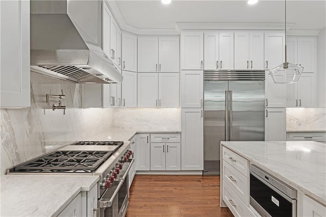 kitchen with hardwood / wood-style flooring, built in appliances, exhaust hood, and backsplash