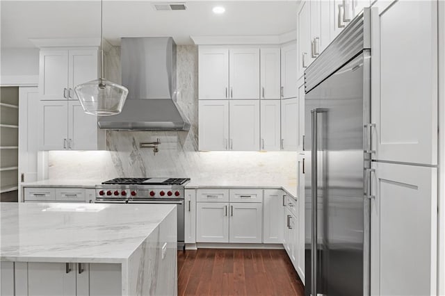 kitchen with high quality appliances, dark wood-type flooring, white cabinetry, light stone counters, and wall chimney range hood