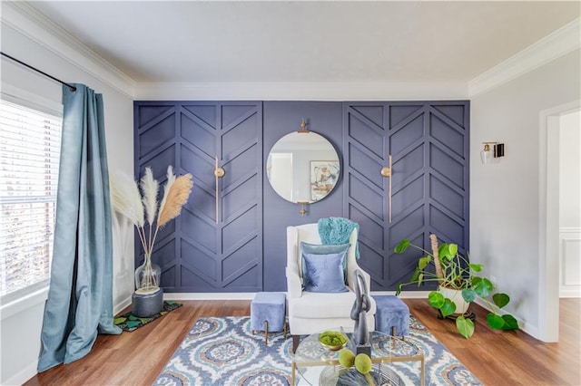 living area with baseboards, a decorative wall, wood finished floors, and crown molding