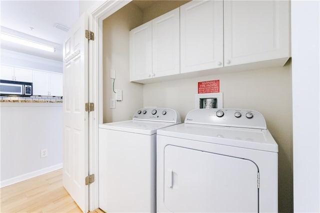 clothes washing area featuring cabinets, light wood-type flooring, washer and clothes dryer, and crown molding