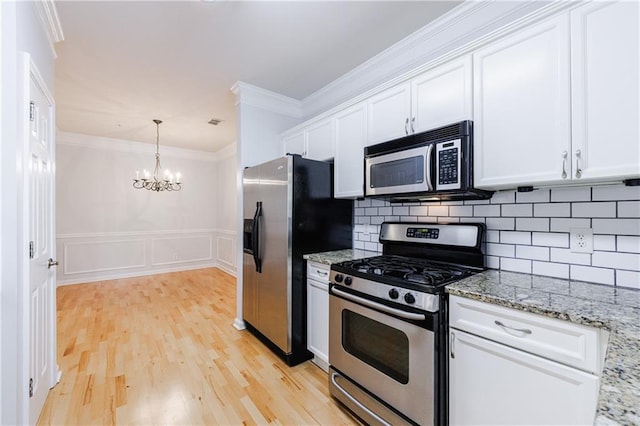 kitchen with light stone counters, ornamental molding, stainless steel appliances, white cabinets, and a chandelier