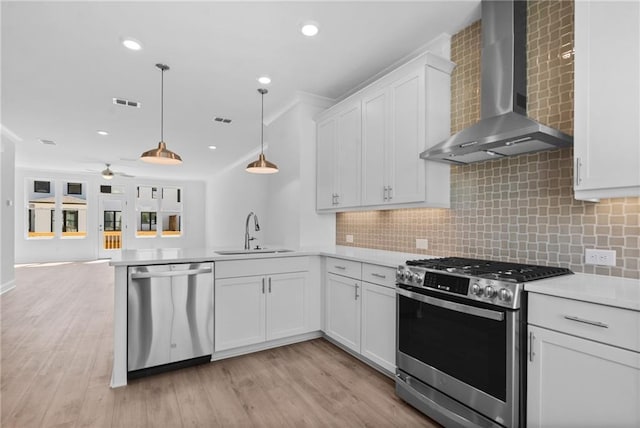 kitchen with a sink, wall chimney range hood, open floor plan, appliances with stainless steel finishes, and a peninsula