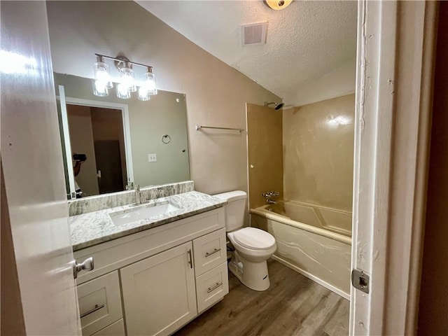 full bathroom with vaulted ceiling, hardwood / wood-style flooring, vanity, tub / shower combination, and a textured ceiling