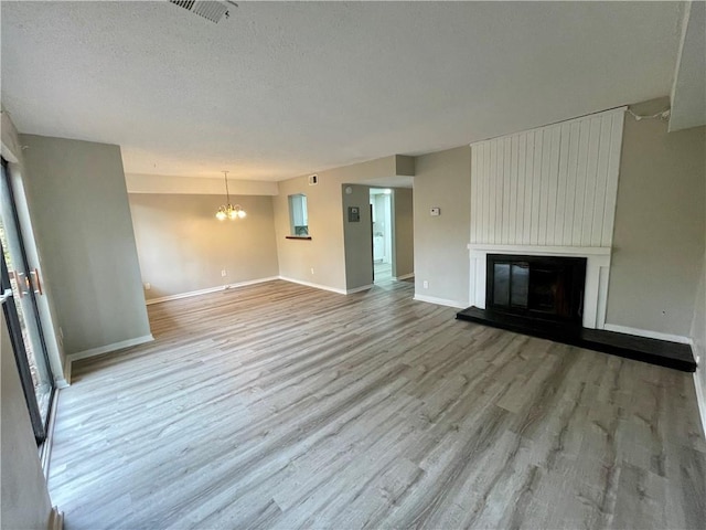 unfurnished living room with a large fireplace, a chandelier, a textured ceiling, and light wood-type flooring