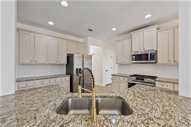 kitchen with light stone countertops, backsplash, stainless steel appliances, sink, and light hardwood / wood-style flooring