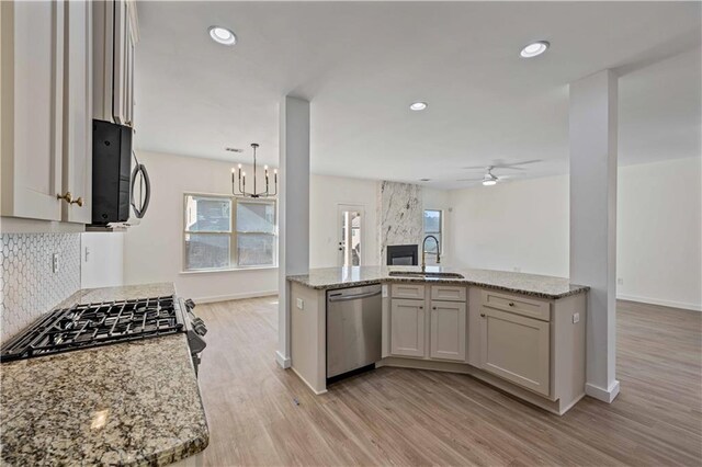 kitchen with light stone counters, ceiling fan with notable chandelier, stainless steel appliances, sink, and light hardwood / wood-style flooring