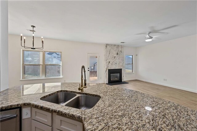 kitchen with a high end fireplace, light stone counters, ceiling fan with notable chandelier, sink, and hardwood / wood-style floors