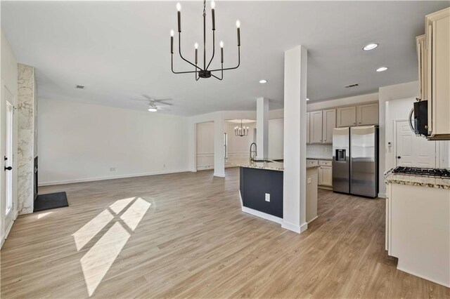 kitchen with appliances with stainless steel finishes, light stone counters, ceiling fan with notable chandelier, cream cabinets, and light hardwood / wood-style floors