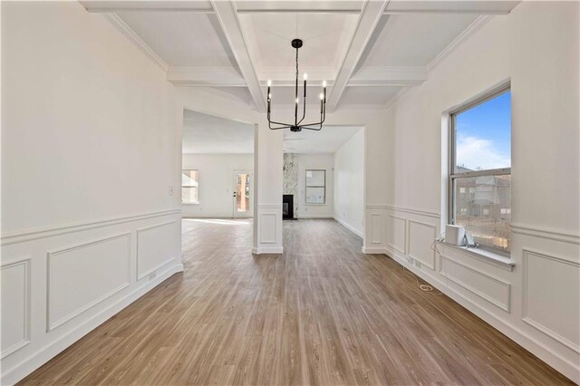 unfurnished dining area featuring light wood-type flooring, coffered ceiling, crown molding, beamed ceiling, and a chandelier