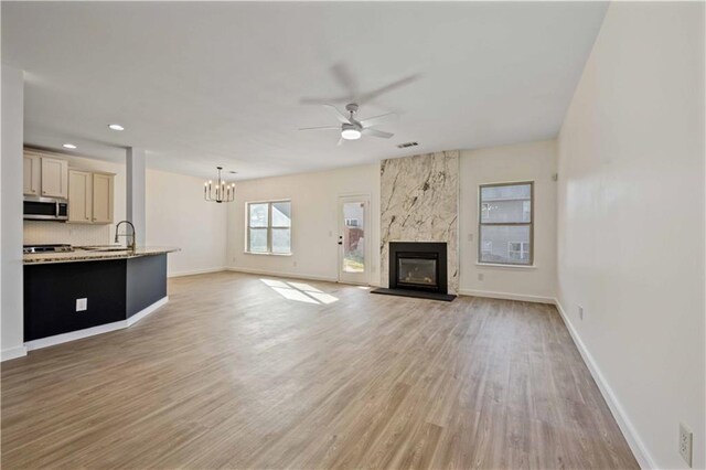 unfurnished living room with light hardwood / wood-style flooring, a high end fireplace, ceiling fan with notable chandelier, and sink