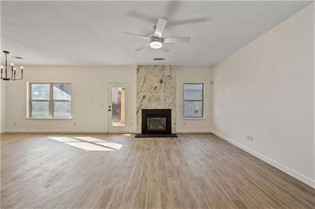 unfurnished living room featuring ceiling fan with notable chandelier, light hardwood / wood-style flooring, and a premium fireplace