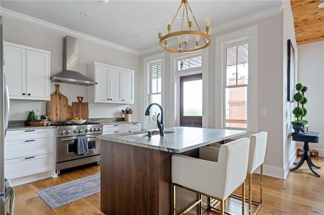 kitchen featuring a sink, white cabinetry, wall chimney range hood, high end range, and a center island with sink