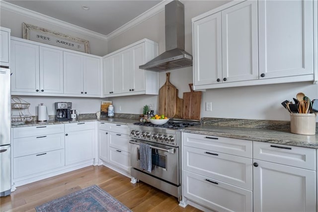 kitchen with high end stove, wall chimney range hood, ornamental molding, and white cabinets