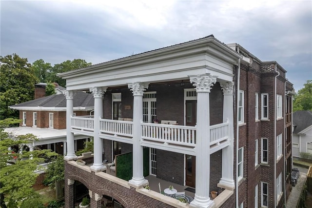 exterior space with a balcony, a chimney, and brick siding