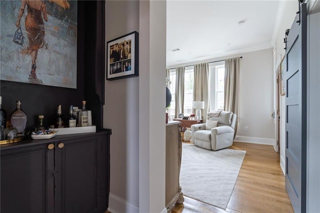 bar featuring crown molding, light wood finished floors, a barn door, a bar, and baseboards