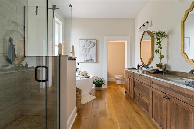 bathroom featuring double vanity, a stall shower, wood finished floors, a freestanding bath, and a sink