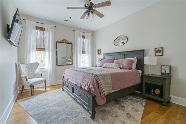 bedroom with a ceiling fan, wood finished floors, visible vents, and baseboards