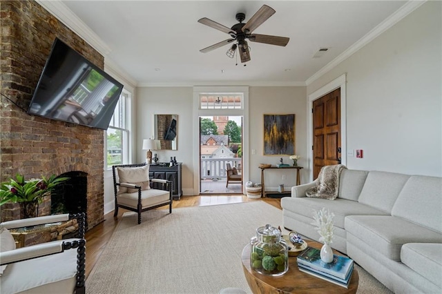 living area featuring a fireplace, wood finished floors, visible vents, a ceiling fan, and ornamental molding