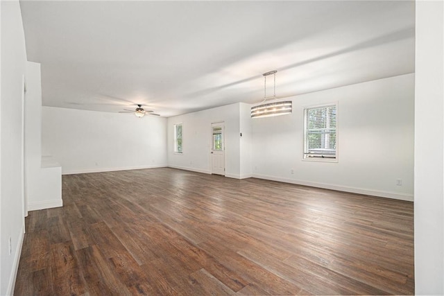 unfurnished living room featuring baseboards, ceiling fan, a healthy amount of sunlight, and dark wood-style floors