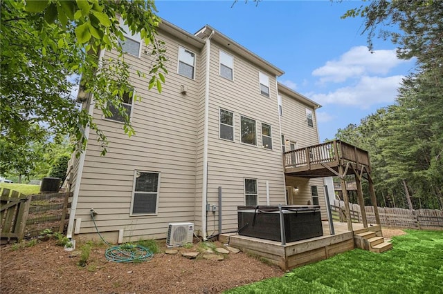 rear view of property with fence, ac unit, a hot tub, a wooden deck, and a lawn