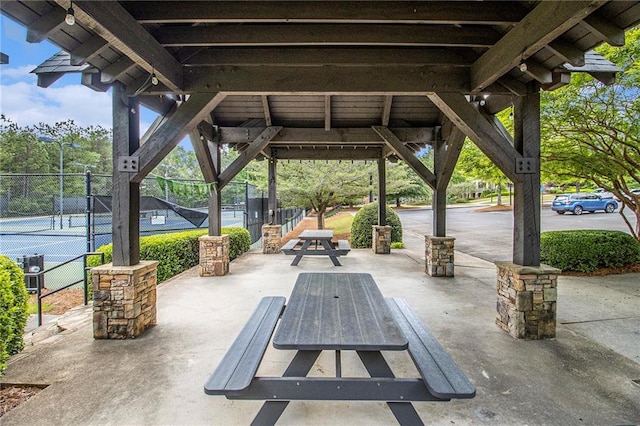 view of patio / terrace featuring a tennis court, fence, and central AC