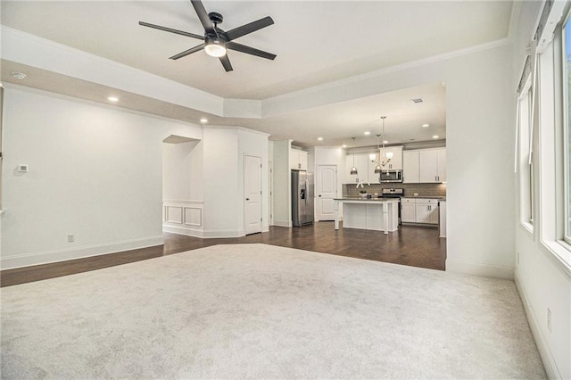 unfurnished living room with crown molding, baseboards, dark carpet, recessed lighting, and ceiling fan with notable chandelier
