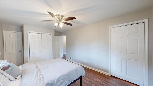 bedroom with multiple closets, dark hardwood / wood-style floors, and ceiling fan