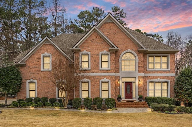 colonial home featuring a front lawn, brick siding, roof with shingles, and a chimney