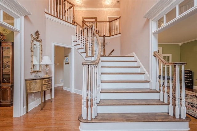 staircase with baseboards, crown molding, a high ceiling, and wood finished floors