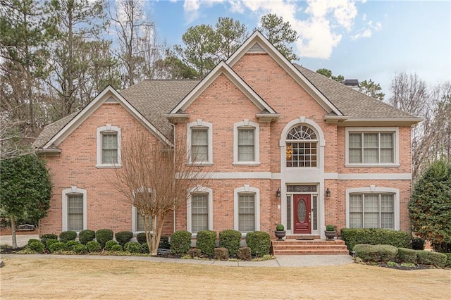 colonial inspired home featuring brick siding, a chimney, a shingled roof, and a front yard